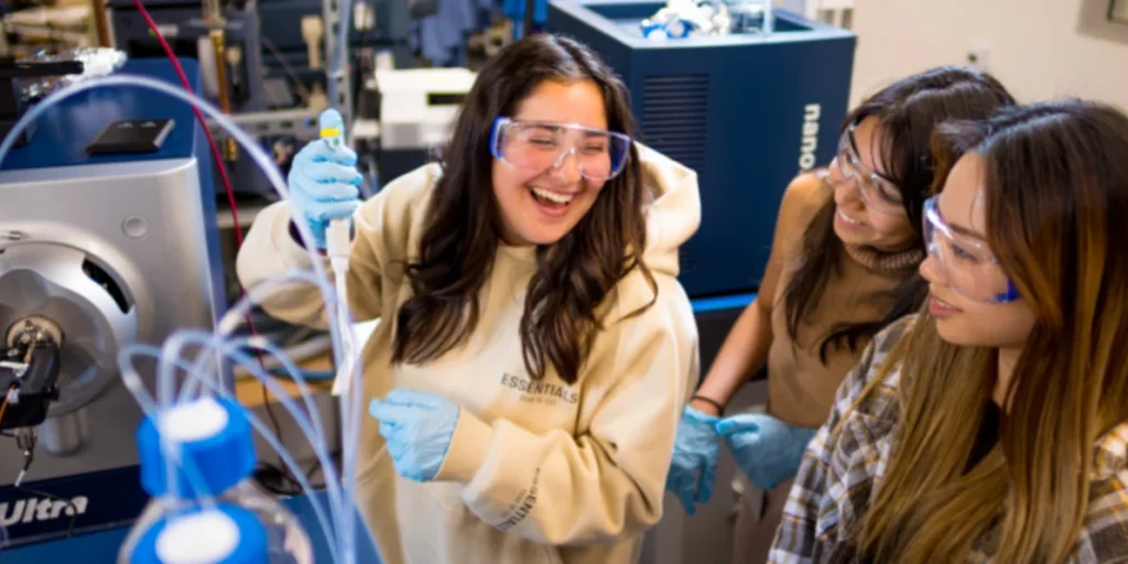 woman in gloves and protective goggles smiling in a lab